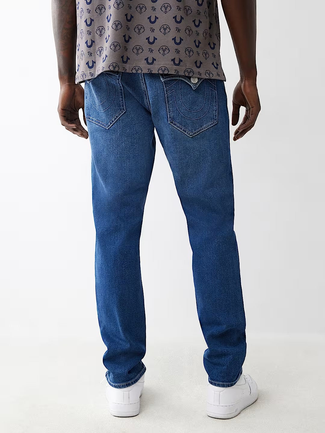 Jeans azules con bolsillos traseros en forma de U, estilo casual, combinados con tenis blancos.